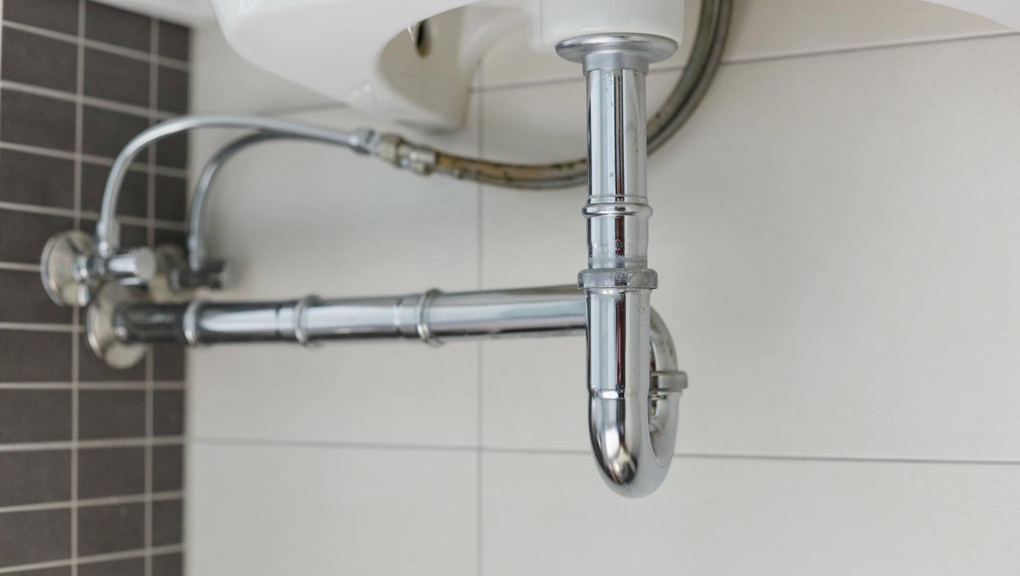 Metallrør og vannledning under en servant, del av baderommets synlige røropplegg.