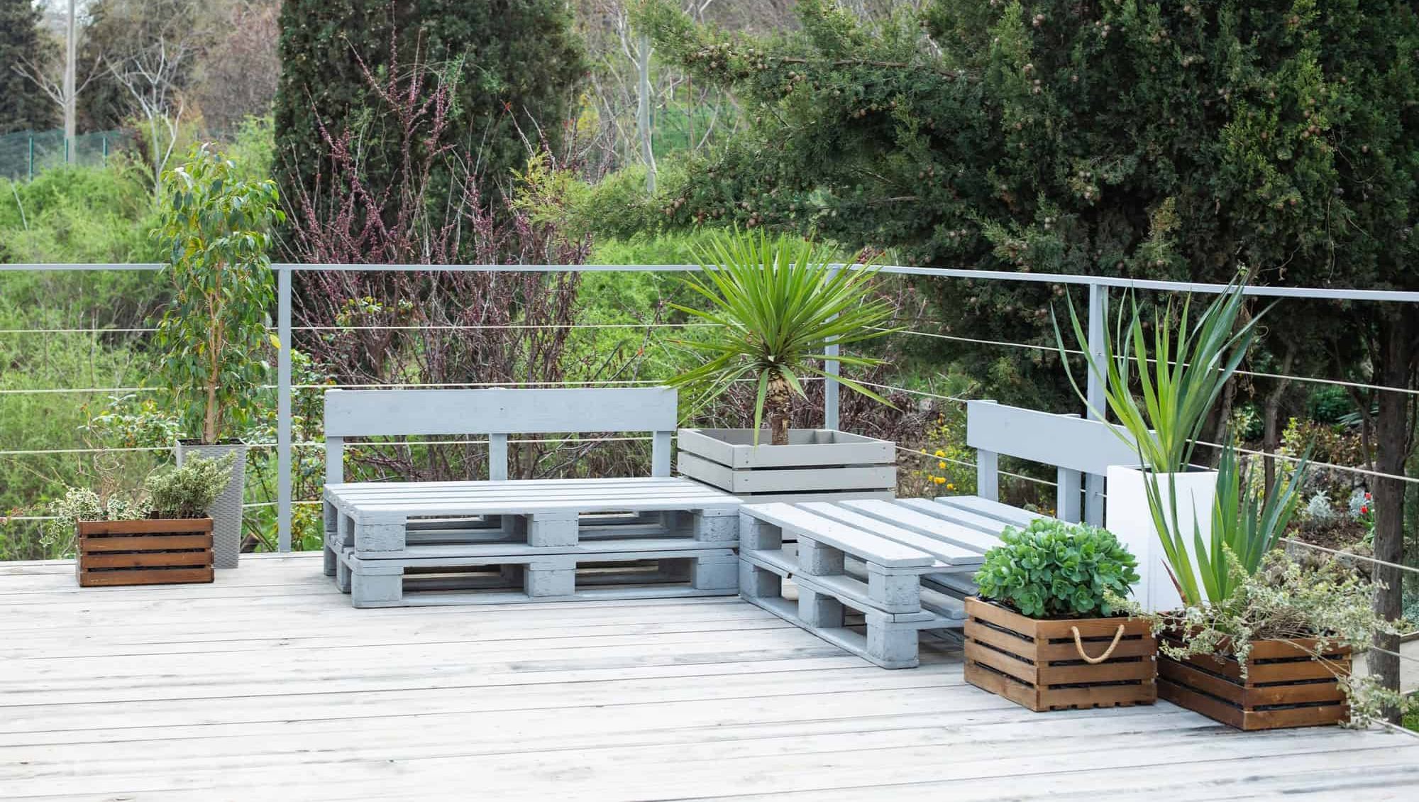 Utemøbler laget av trepaller står på en terrasse med blomsterkasser og grønne planter.