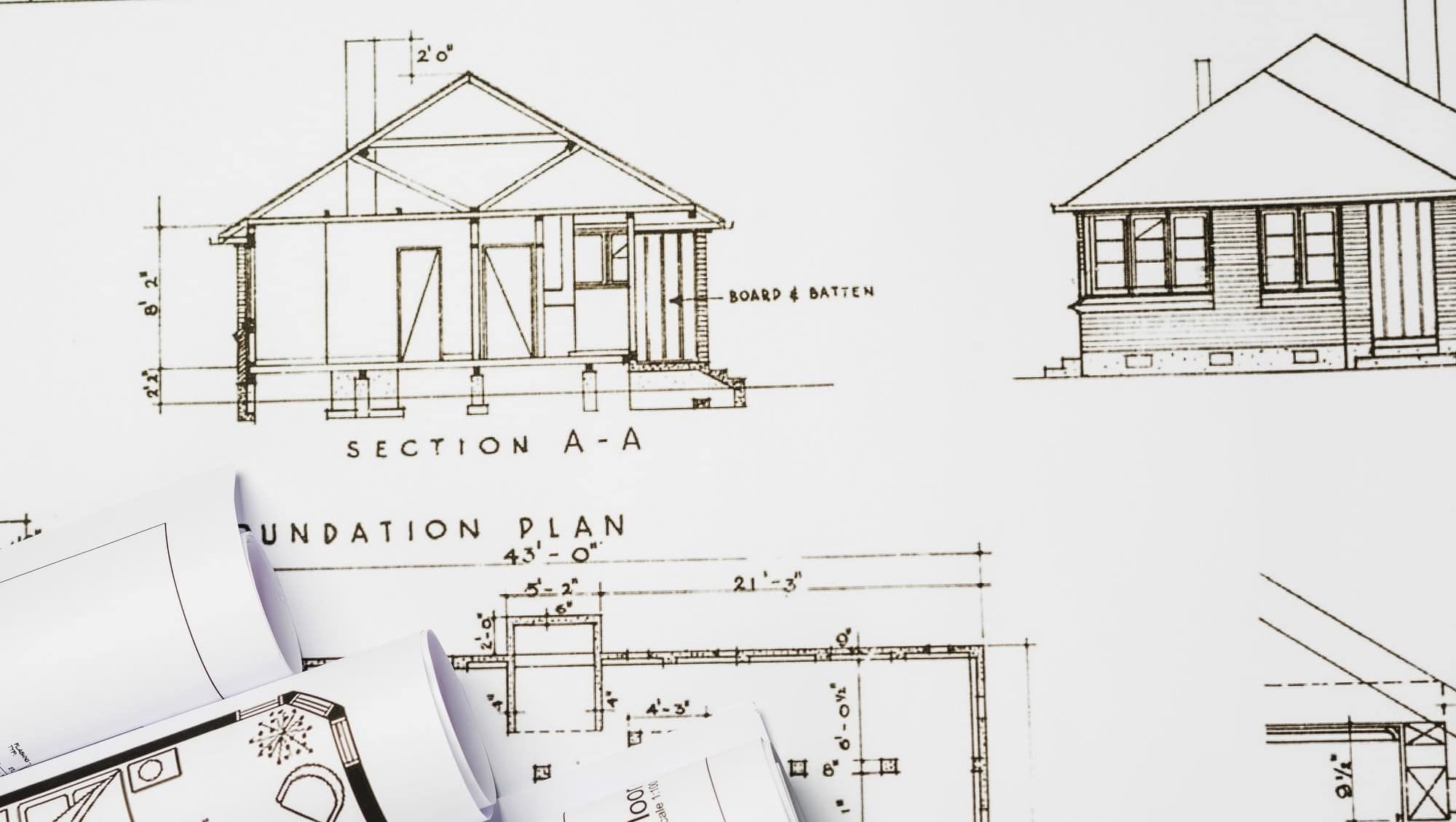 Arkitekttegning av husplan med mål, snitt og plantegninger, sammenrullet papir i forgrunnen.