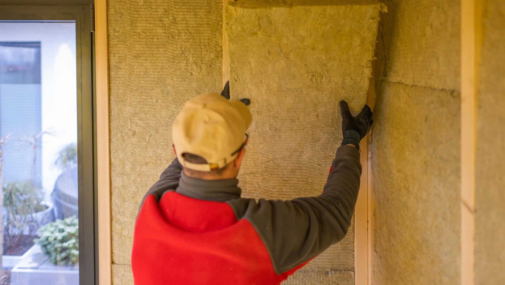 En håndverker monterer isolasjonsplater i en trekonstruksjon for å sikre god varmeisolasjon.